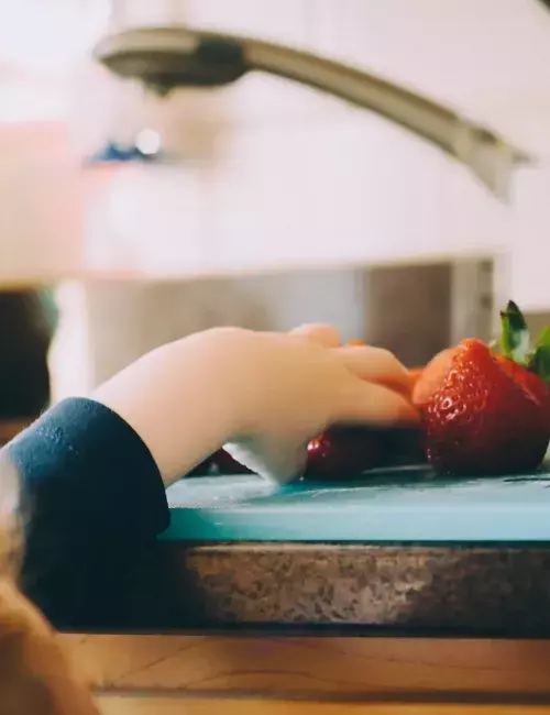small child reaching for a strawberry on a kitchen counter