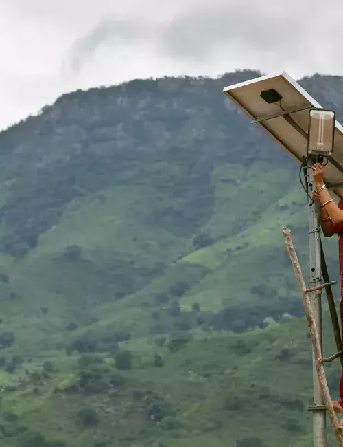 Woman adjusting a solar panel in Africa, with mountains behind